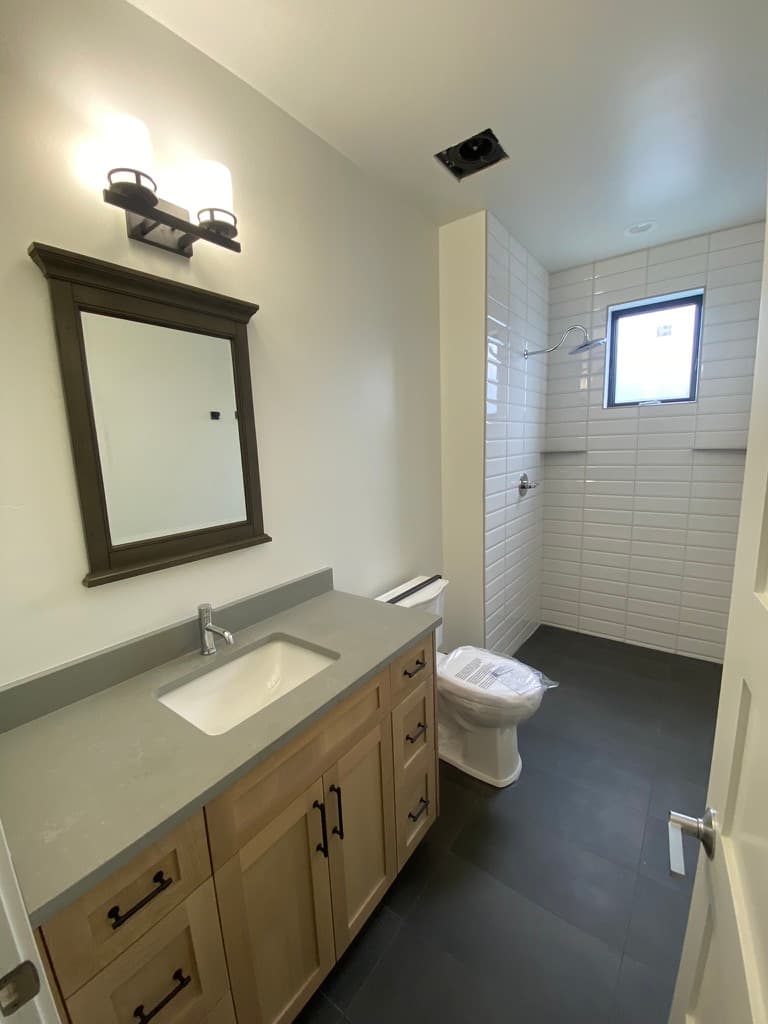 Bathroom with a light wood vanity, a gray counter, and a white subway-tile shower