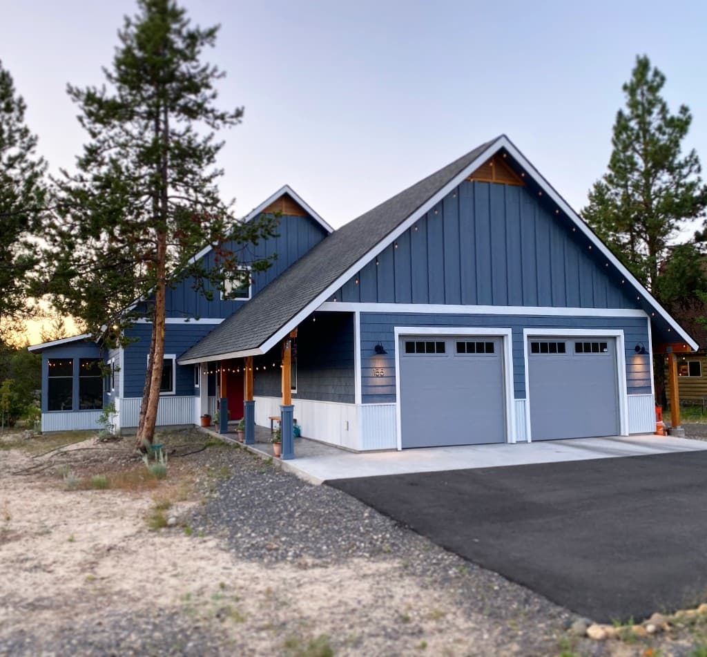 Blue gabled residence with white trim, a covered entry, and two garage doors