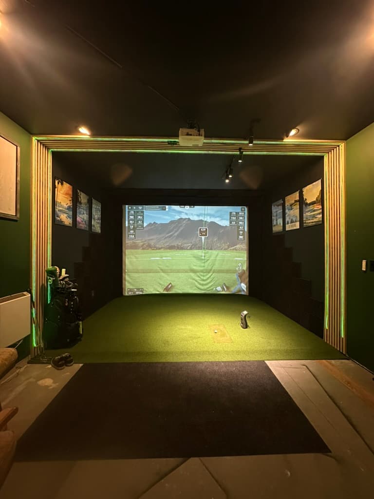 Indoor golf simulator with a projection screen, turf, and wood slat surround