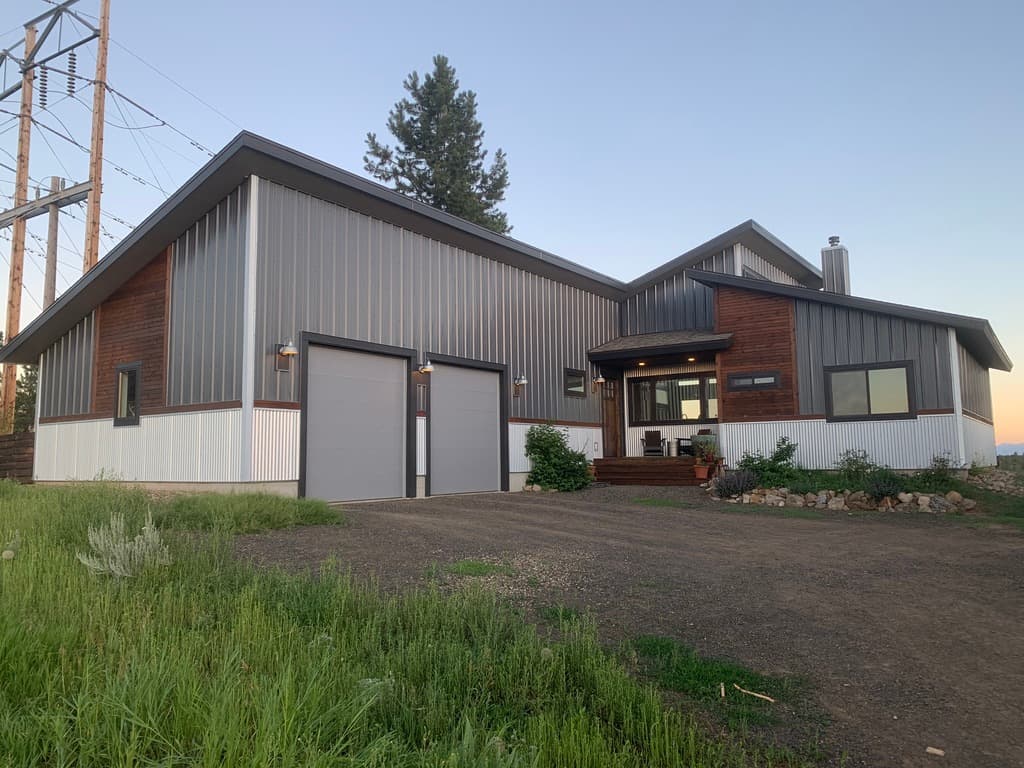 Custom residence with gray metal siding, wood accents, a white metal wainscot, and an attached garage