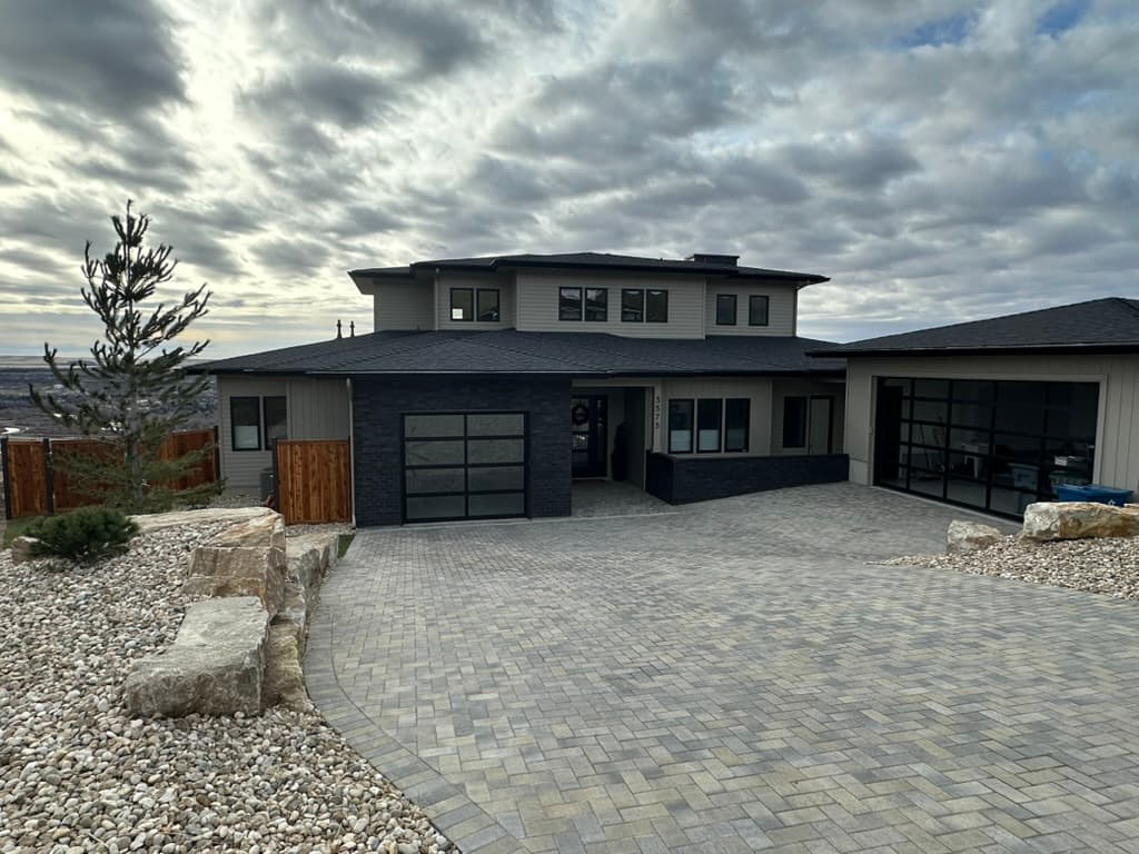 Gray custom residence with a dark stone garage front and a paver driveway