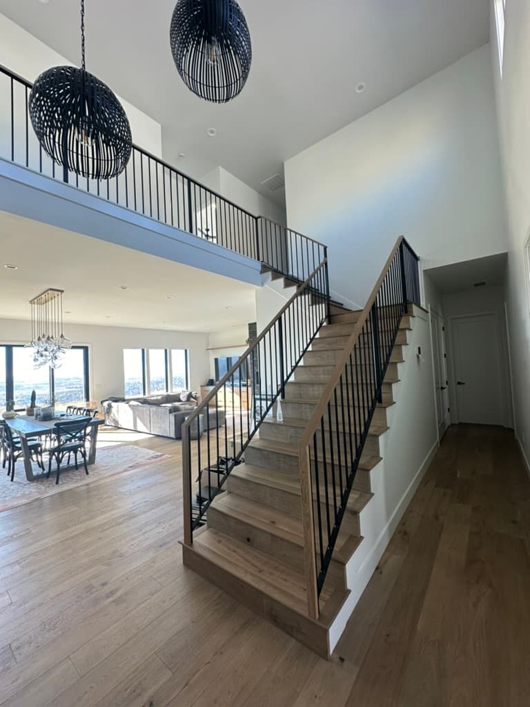 Two-story great room with a wood stair, black metal rail, and a view through tall windows