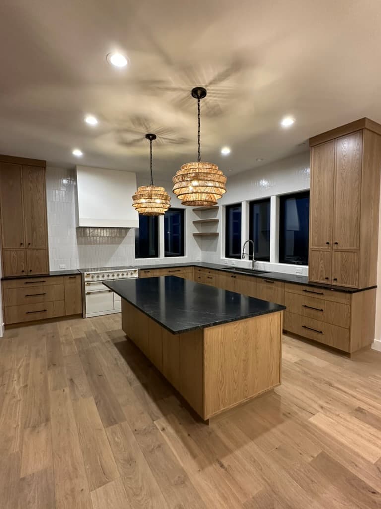 Kitchen with light wood cabinets, a dark stone island, and woven pendants